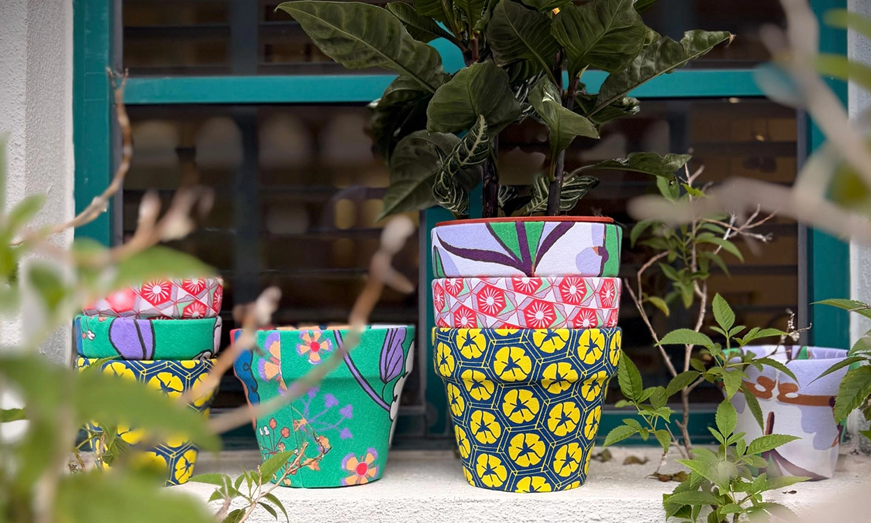 pot-new-1 A row of fabric-covered terracotta pots in bold nala prints, stacked and planted, on a sunny windowsill.