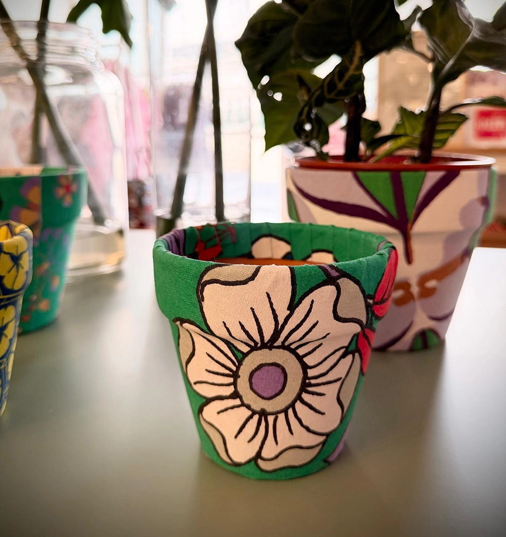 pot-new-2 A small terracotta pot wrapped in green fabric with a large cream flower print, beside a lilac and purple pot.