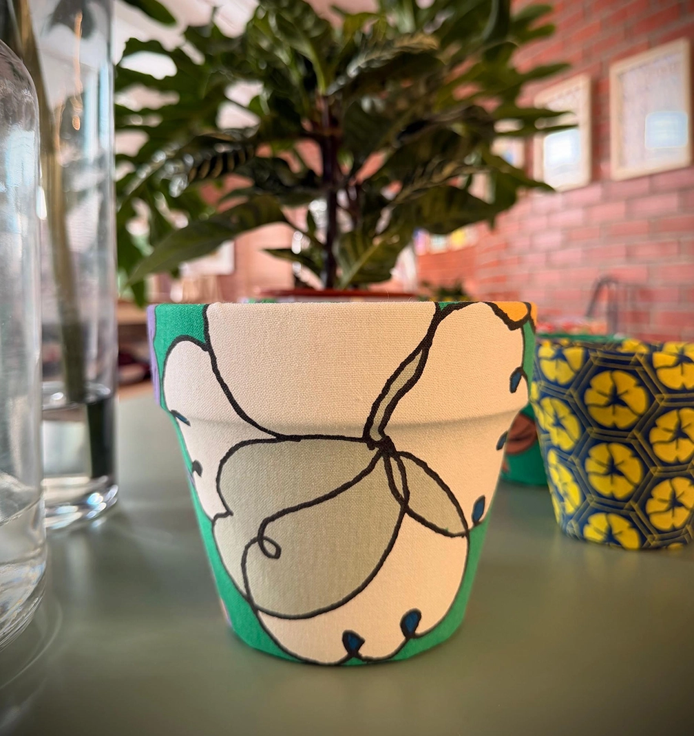 pot-new-5 A cream and green floral fabric pot holding a leafy plant, with a navy and yellow pot against a brick wall.